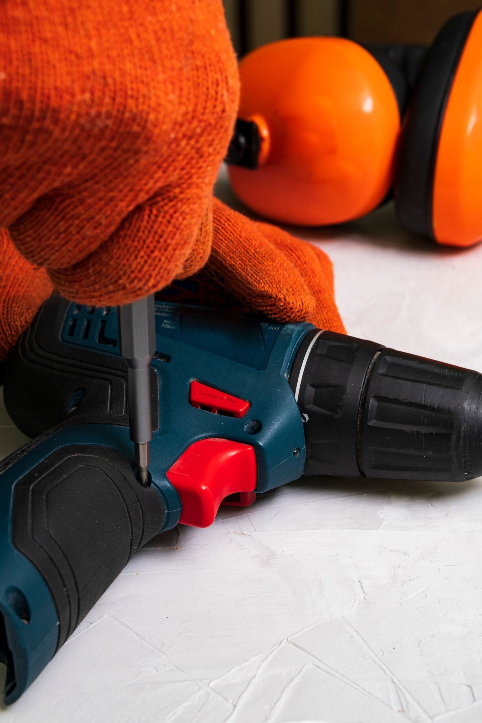 Detailed view of a power drill on a workbench with safety gloves and ear protection.