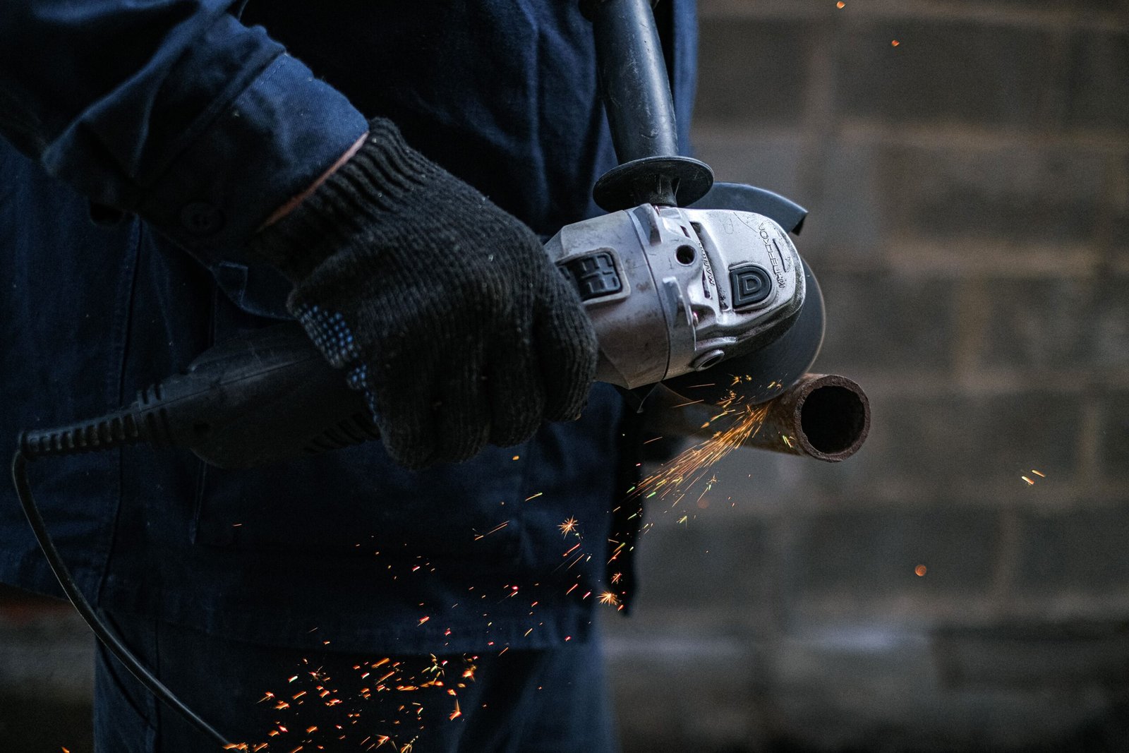 A person uses a grinder on metal, creating sparks, indicating metalwork or repair activity.